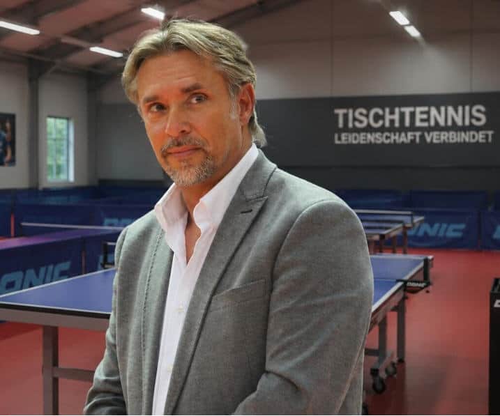 Tischtennisspieler im Training in Leonding, Österreich, mit Tischtennisplatten im Hintergrund.