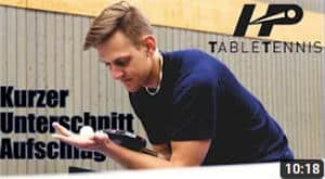 Junger Mann demonstriert Tischtennistechnik: Perfekter kurzer Unterschnitt-Aufschlag in Sporthalle.