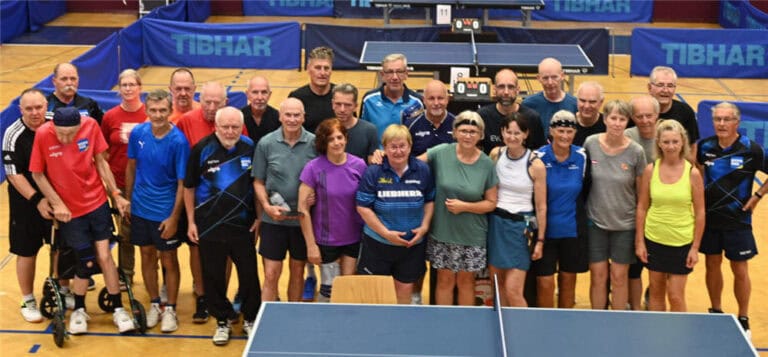 Gemeinschaftliches Tischtennis-Event: Erwachsene aller Altersgruppen in Sportbekleidung posieren lächelnd zusammen.