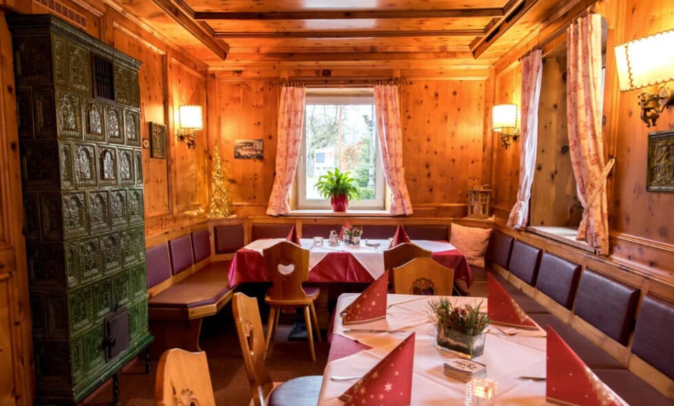 Gemütliches Alpen-Esszimmer aus Holz mit Kachelofen, festlichem Tisch und herzförmigen Stühlen.