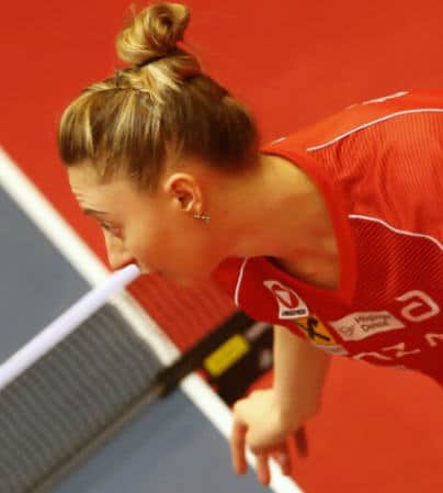 Konzentrierte Tischtennisspielerin in rotem Trikot während eines professionellen Matches.