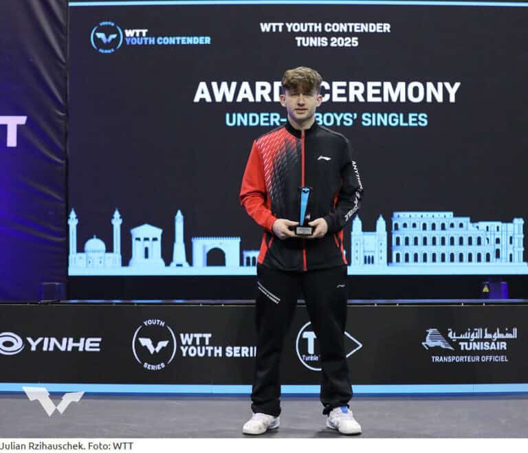 Junger Tischtennisspieler gewinnt bei WTT-Turnier in Tunis, hält Trophäe, stolz auf der Bühne.