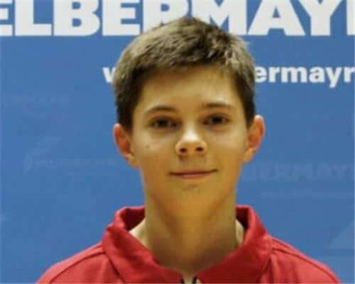 Junger Teenager in roter Jacke vor ELBERMAYR-Blau hinter neutralem Gesichtsausdruck.