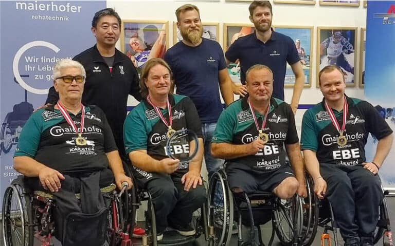 Erfolgreiche Rollstuhlsportler feiern mit Trainern, Medaillen und Trophäe in grün-schwarzen Team-Uniformen.